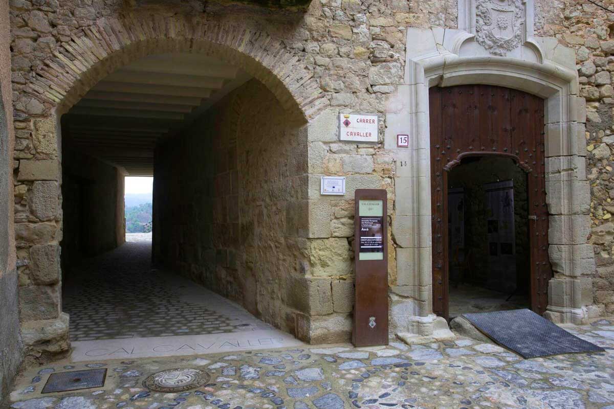Carrer cavaller on hi ha ubicada una entrada a una casa antiga on a la façana es veuen detalls de pedra