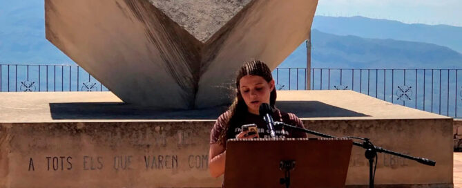 Acte d'Homenatge a víctimes i Combatents de la Batalla de l'Ebre, on una noia està llegit unes paraules, i al darrere hi ha el monument en homenatge a totes les víctimes.