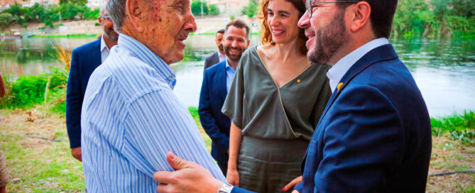 Pere Aragonès i un senyor saludant-se amb la mà, mentrestant al darrere hi ha persones mirant com se saluden i estan somrient.