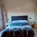 Fotografia d'una habitació amb un llit de matrimoni, dues tauletes de nit de color blanc i dues columnes de pedra vista.