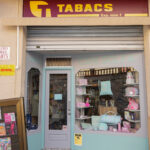 Part exterior de la tenda Can Solfa, on es veu la porta de la tenda oberta i un aparador il·luminat on hi ha diferents productes, bosses de mà, perfums...