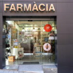 Entrada d'un negoci. On es veu un rètol on posa farmàcia ben gran i una porta corredissa de vidre.