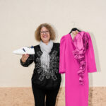 Dona posant amb una sabata blanca amb detalls blau fosc a la mà dreta i un vestit de color rosa a la mà esquerra.